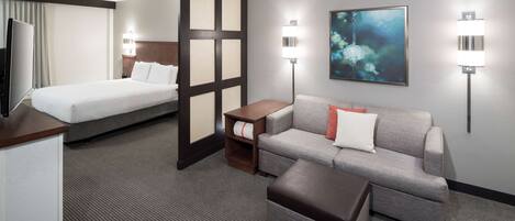 A hotel room with a bed, a sofa, a coffee table, and a TV.