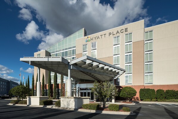 A modern hotel with a covered entrance, large windows, and a clear sky.