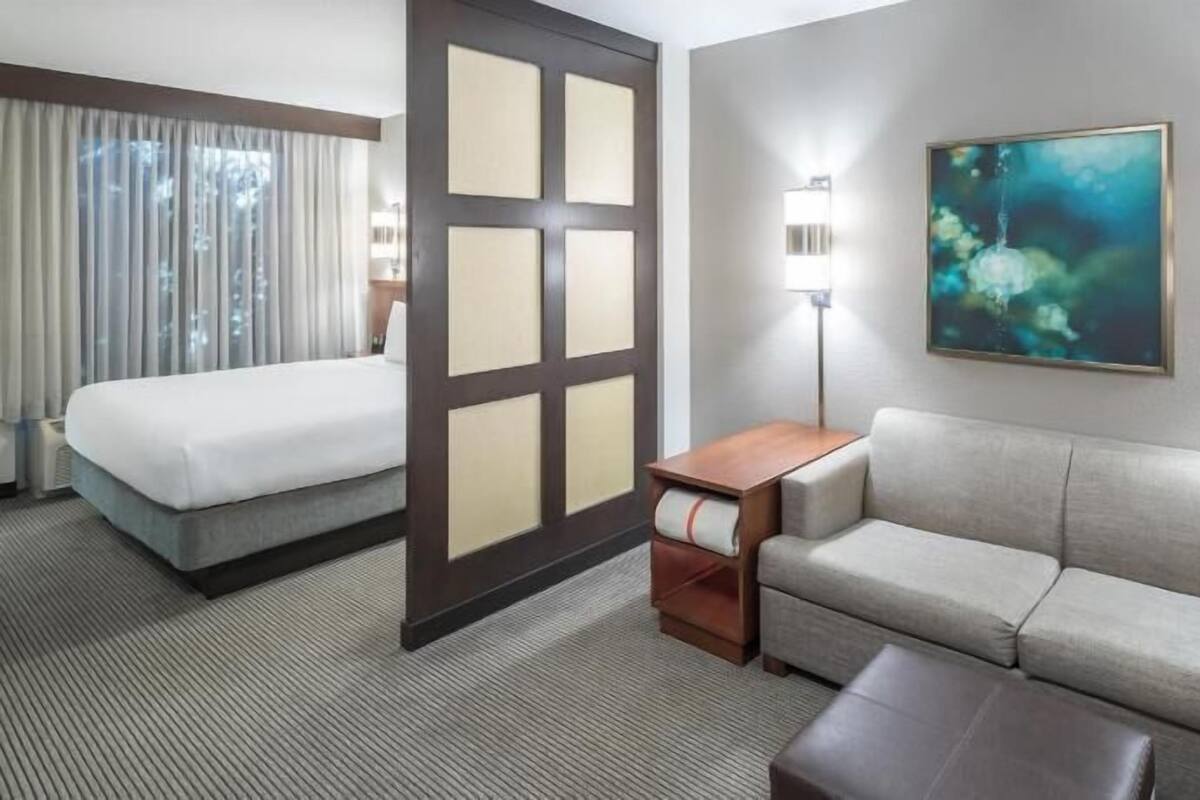 Ein Hotelzimmer mit Bett, Sofa, kleinem Tisch, Lampe und einem Bild an der Wand.