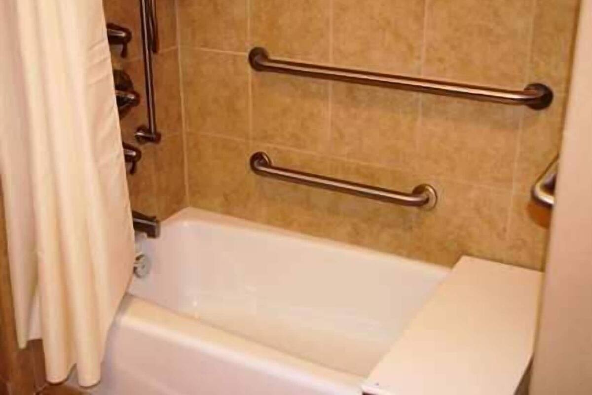 Un bagno con una vasca, due mancorrenti e una tenda per la doccia.