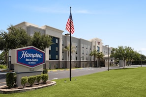 Edificio de un Hampton Inn & Suites by Hilton, cielo despejado, estacionamiento y una bandera.