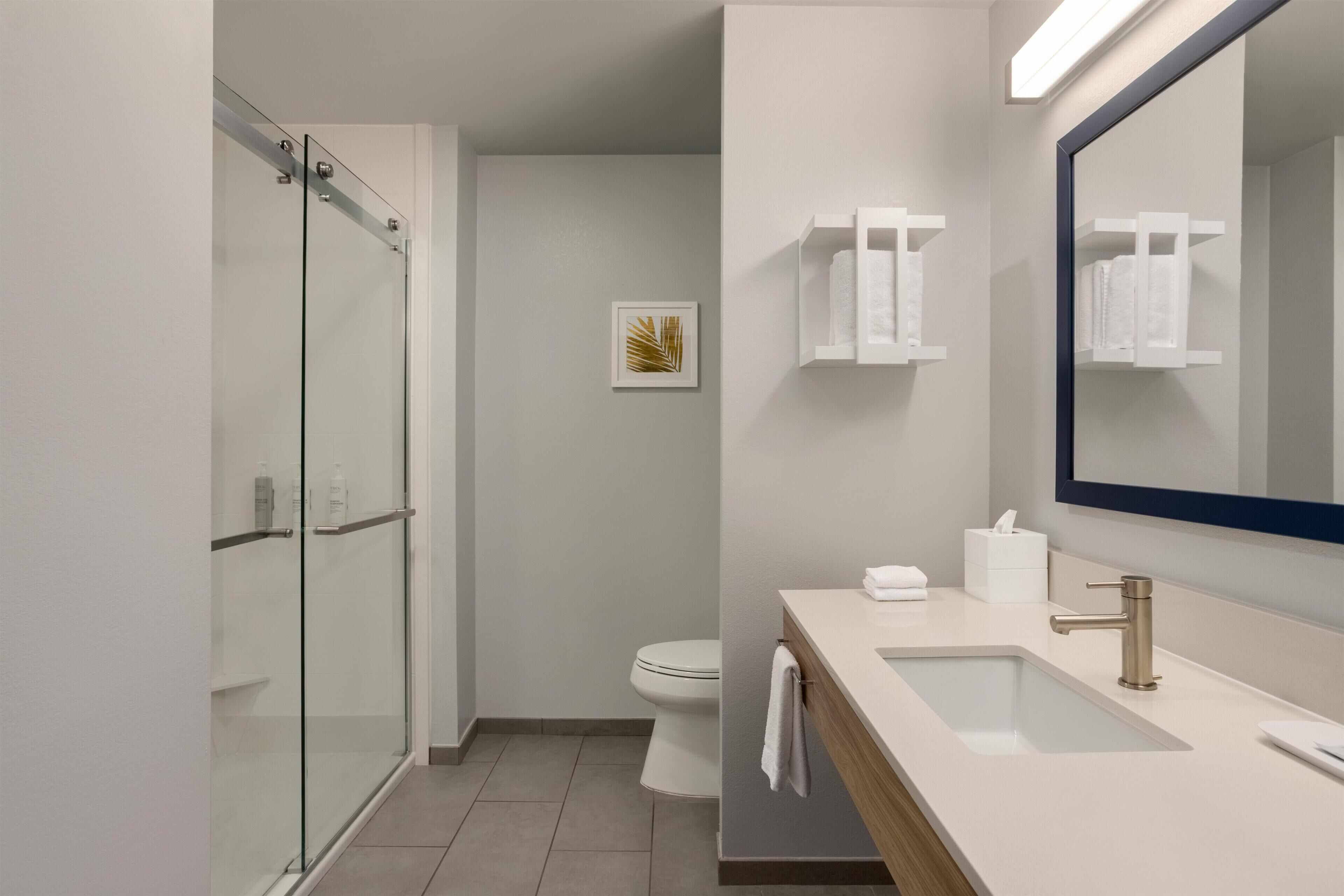 A modern bathroom with a glass shower enclosure, a toilet, a sink with a mirror, and a towel rack.