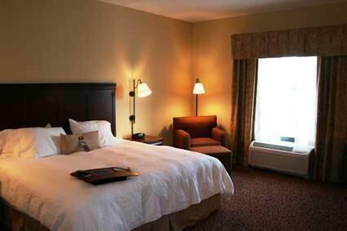 Una camera d'albergo con un letto, due abat-jour, una sedia e un'ampia finestra.