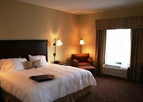 A hotel room with a large bed, two bedside lamps, a chair, and a window with curtains.