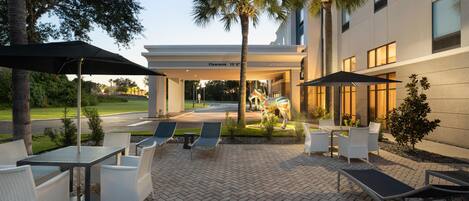 An outdoor patio area with seating and umbrellas, a clear sky, and a building entrance with a 'Welcome' sign.
