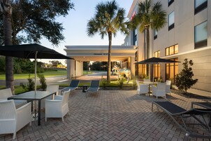 An outdoor patio area with seating and umbrellas, a clear sky, and a building entrance with a 'Welcome' sign.