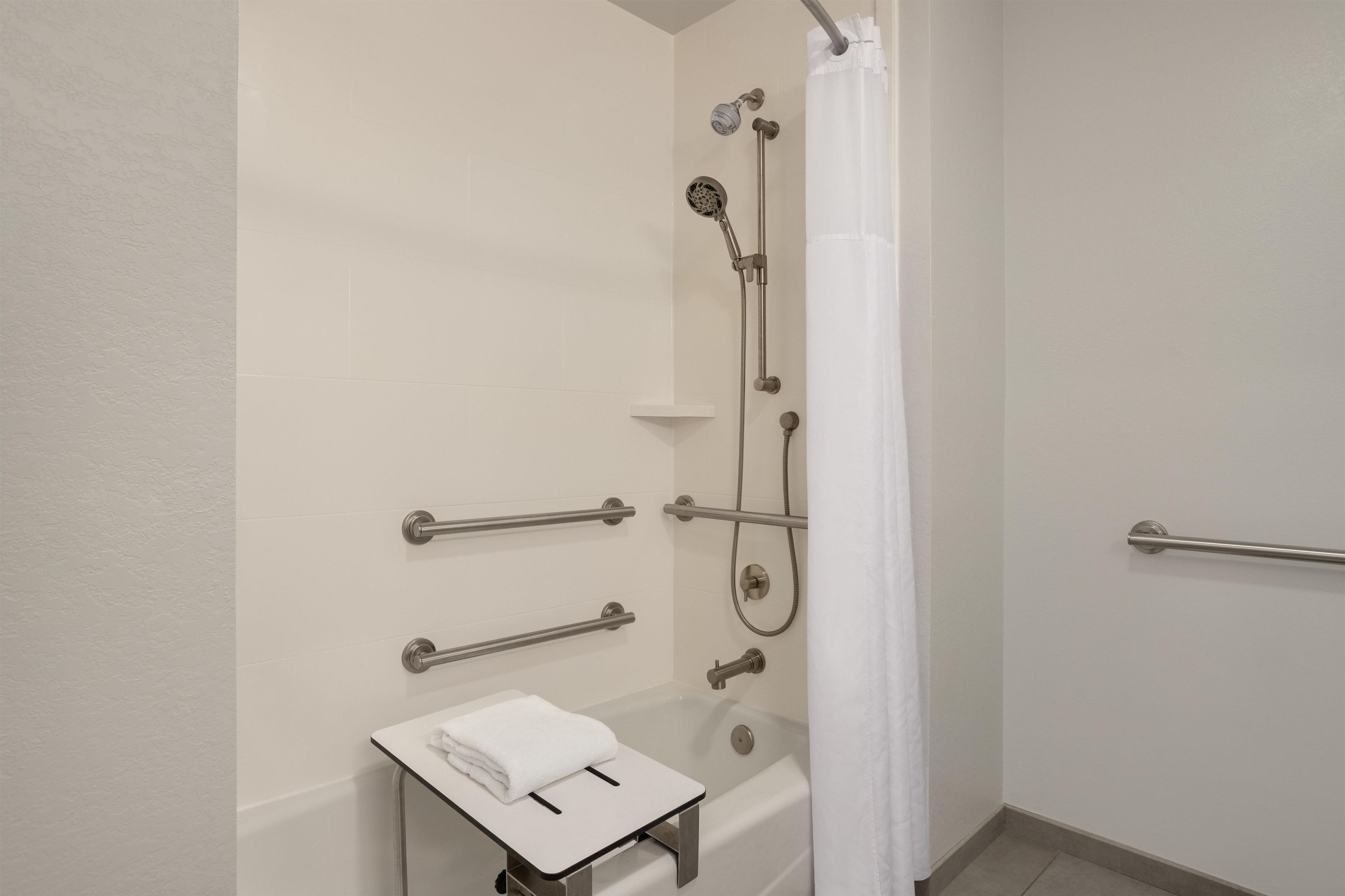 Een moderne badkamer met een inloopdouche, handgrepen, een handdoekhouder en een toilet met een handdoek.
