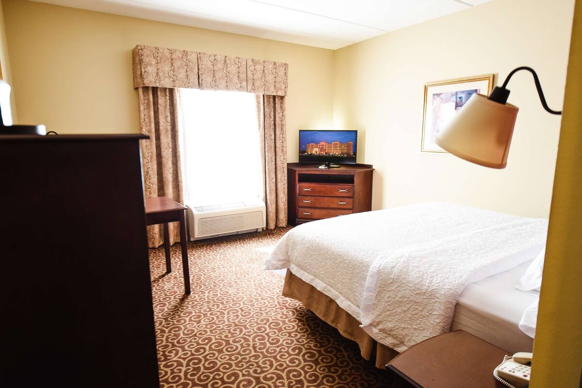 Una camera d'albergo con un letto, una cassettiera, un televisore e una lampada.