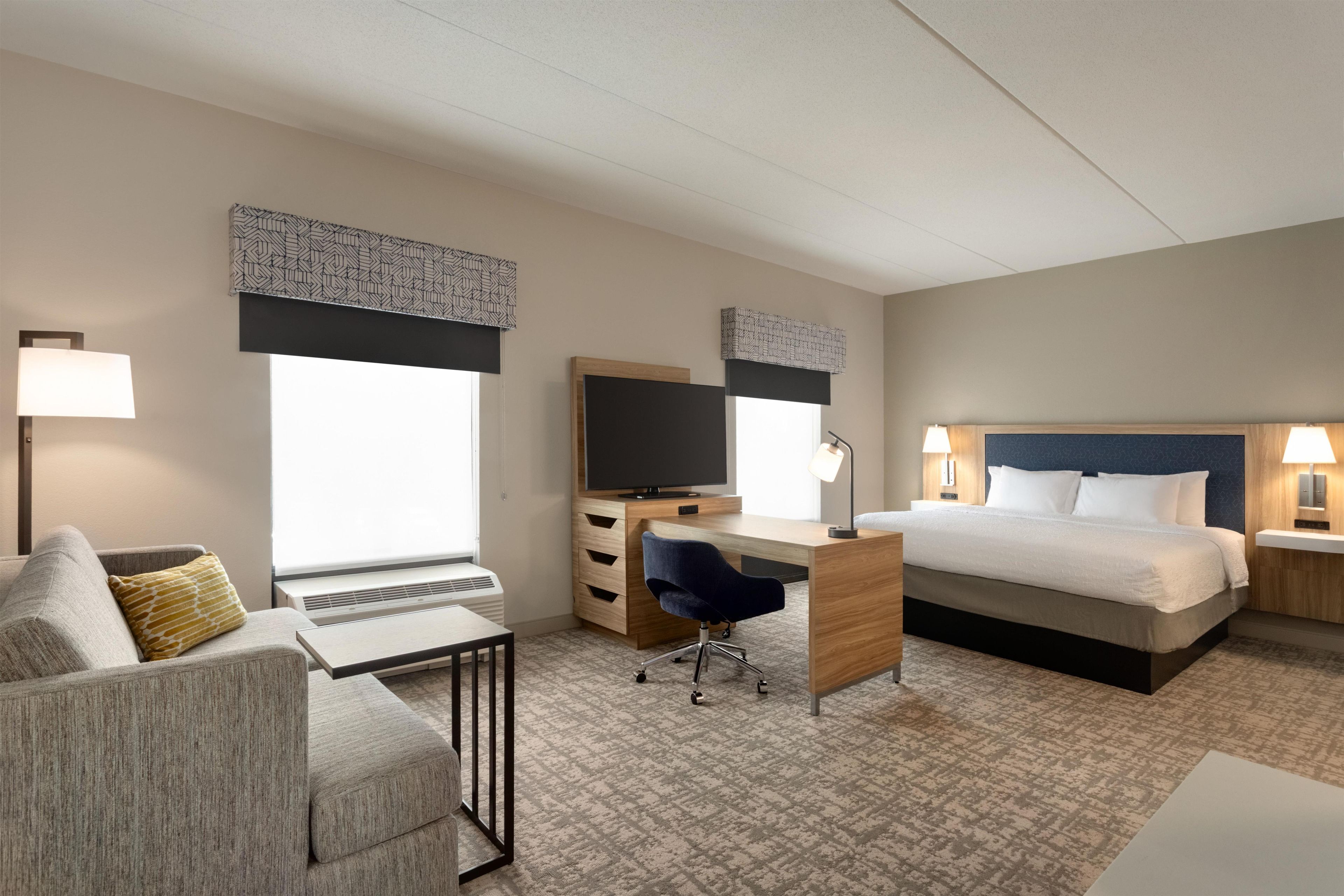 A hotel room with a bed, a desk, a chair, a television, and a lamp.