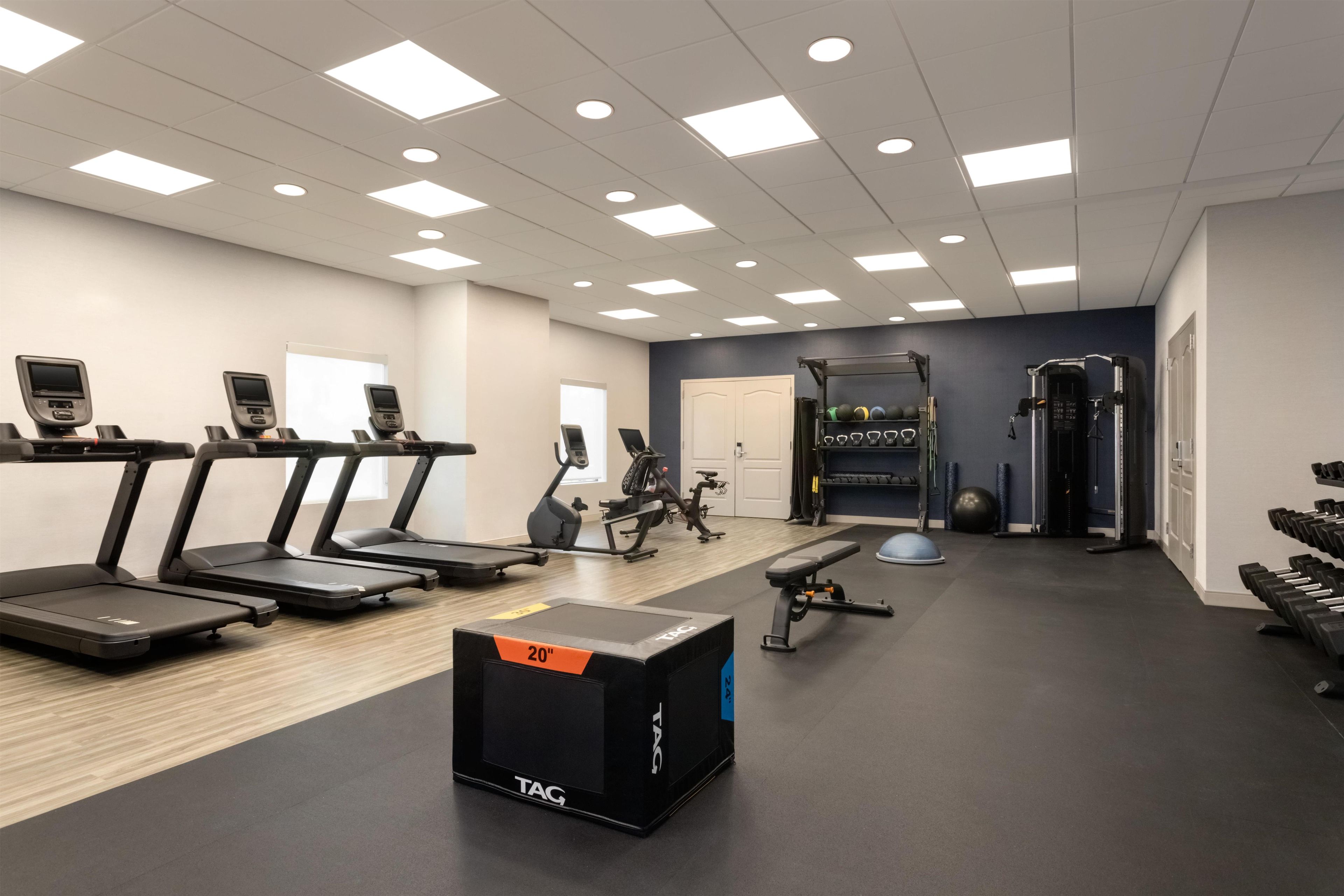 Une salle de sport équipée de tapis de course, de vélos d’appartement, d’un support à squats et de poids libres.