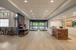 A reception area with a wooden reception desk, a seating area with bar stools, and a wall-mounted coffee machine.