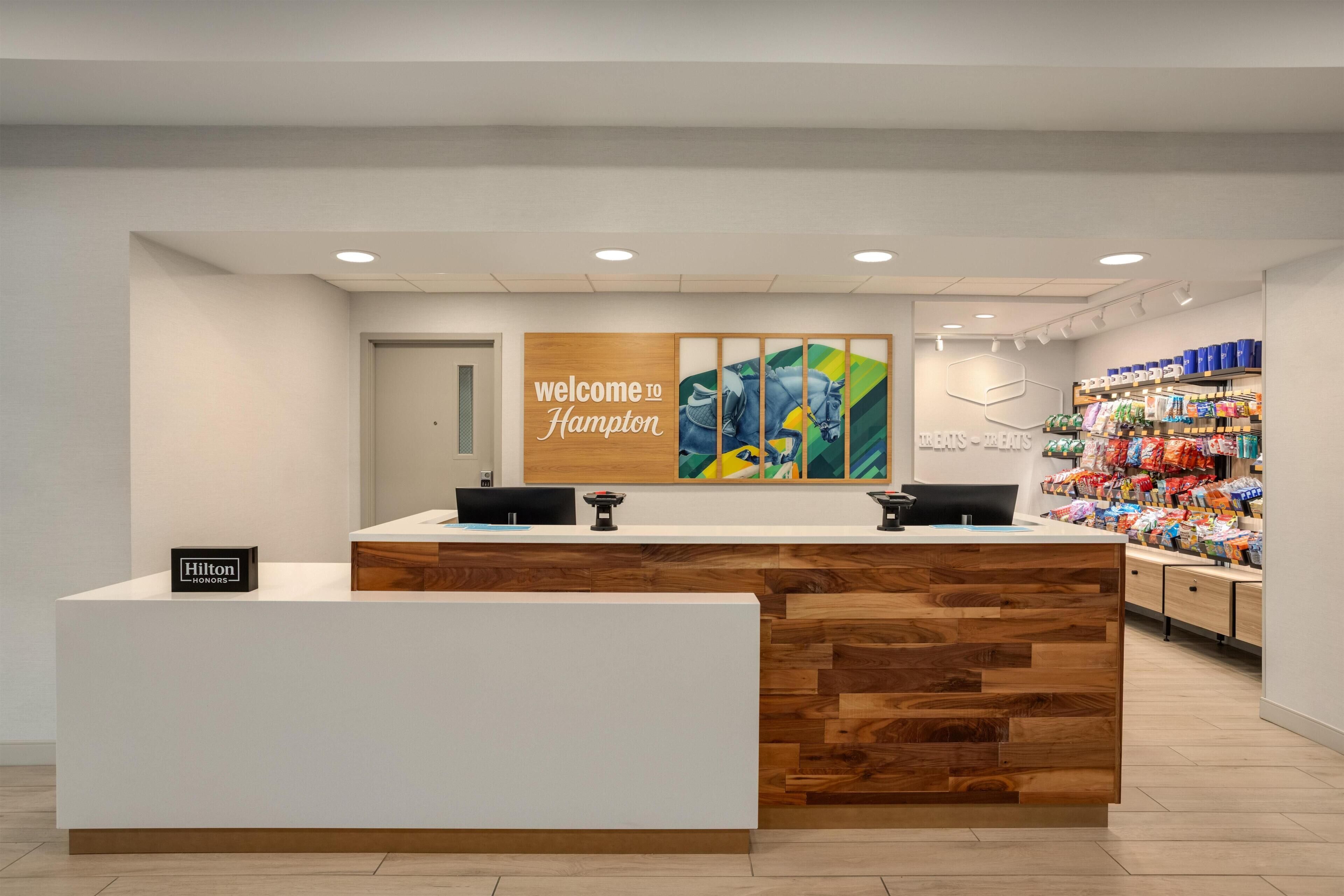 Una recepción con un cartel de 'welcome to Hampton', un cartel de 'Hilton Honors' y una pared con una pintura de un caballo colorido.