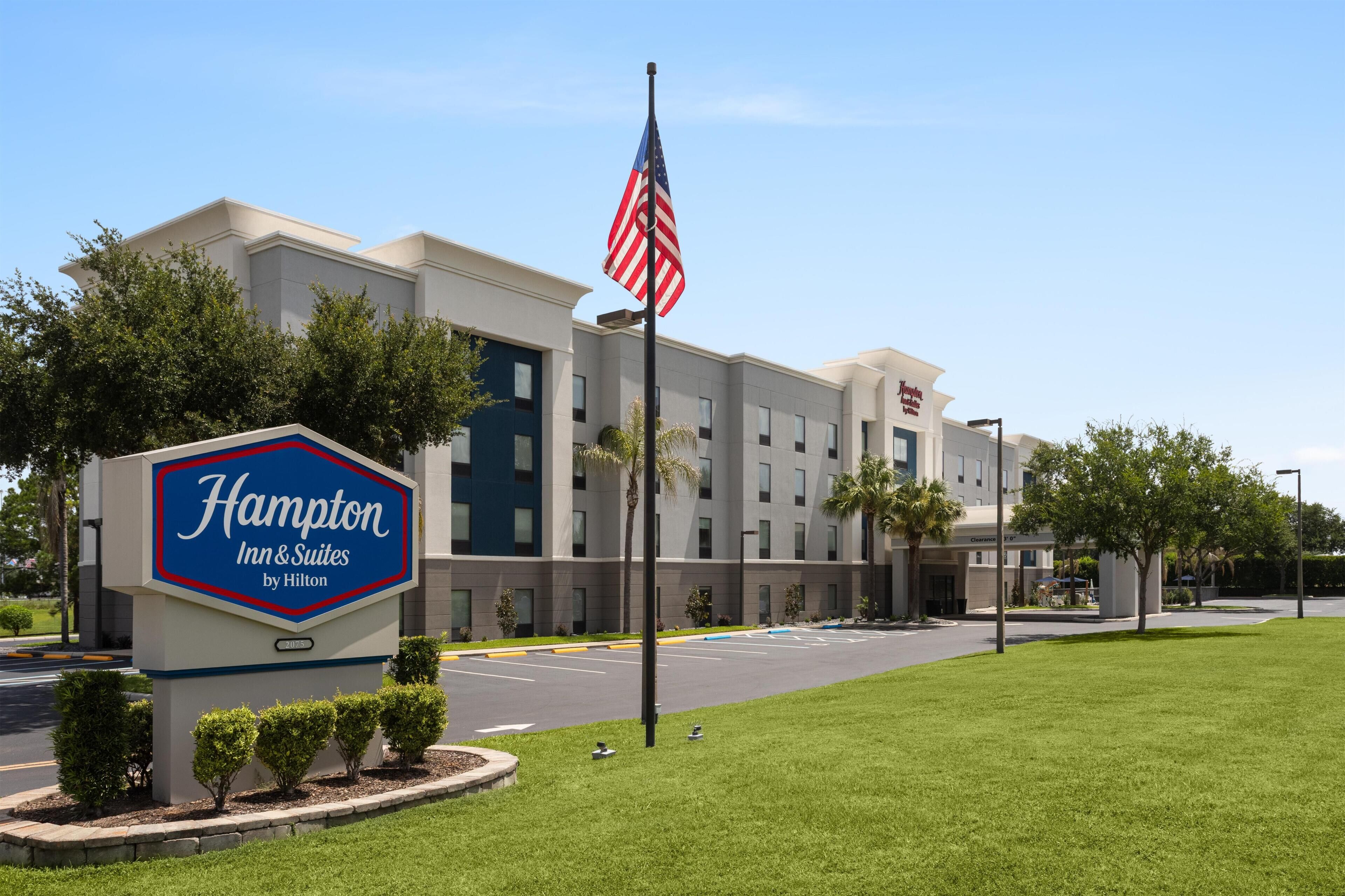 A Hampton Inn & Suites by Hilton building with a clear sky, parking lot, and a flag.