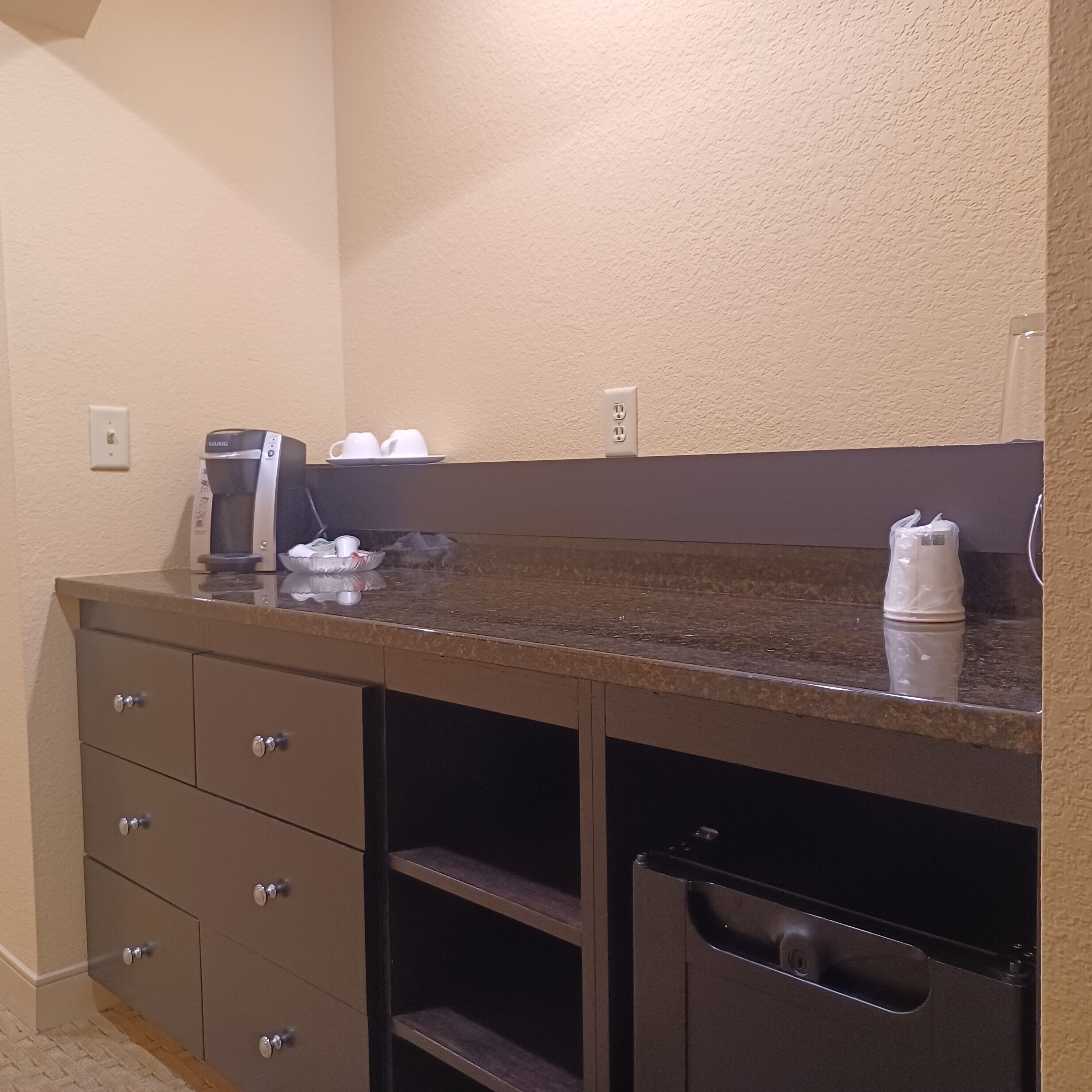A kitchenette with a coffee maker, a sink, and a trash bin.