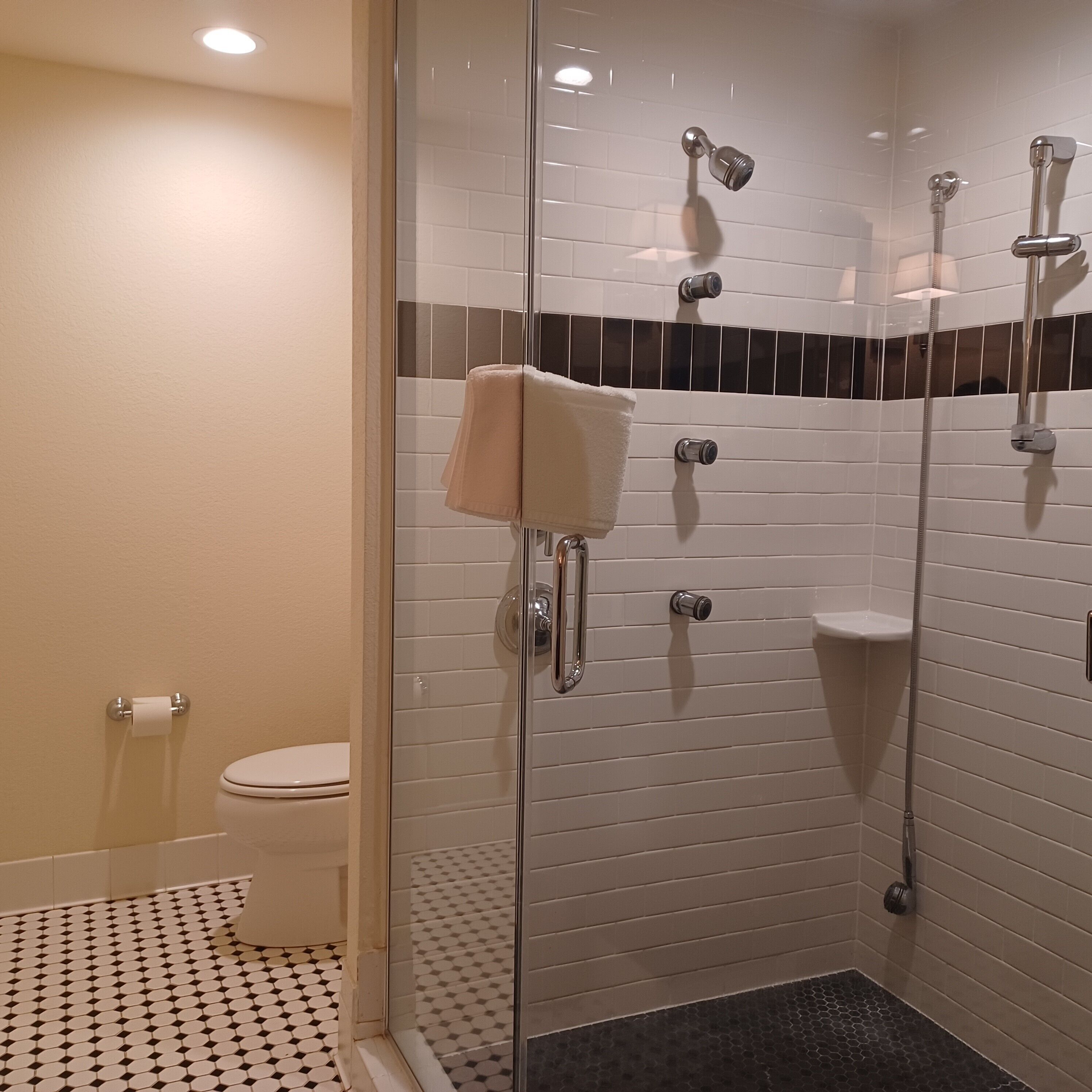 A modern bathroom with a glass-enclosed shower, white tiled walls, a toilet, and a patterned floor.