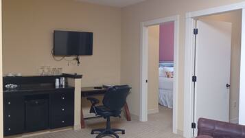 A hotel room with a desk, chair, television, bed, and a brown leather sofa.