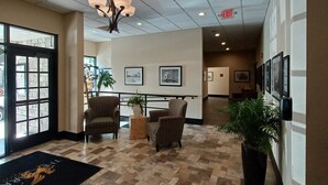 Un hall d’entrée avec un lustre, deux fauteuils, une plante en pot, des tableaux encadrés au mur et un panneau indiquant la sortie.
