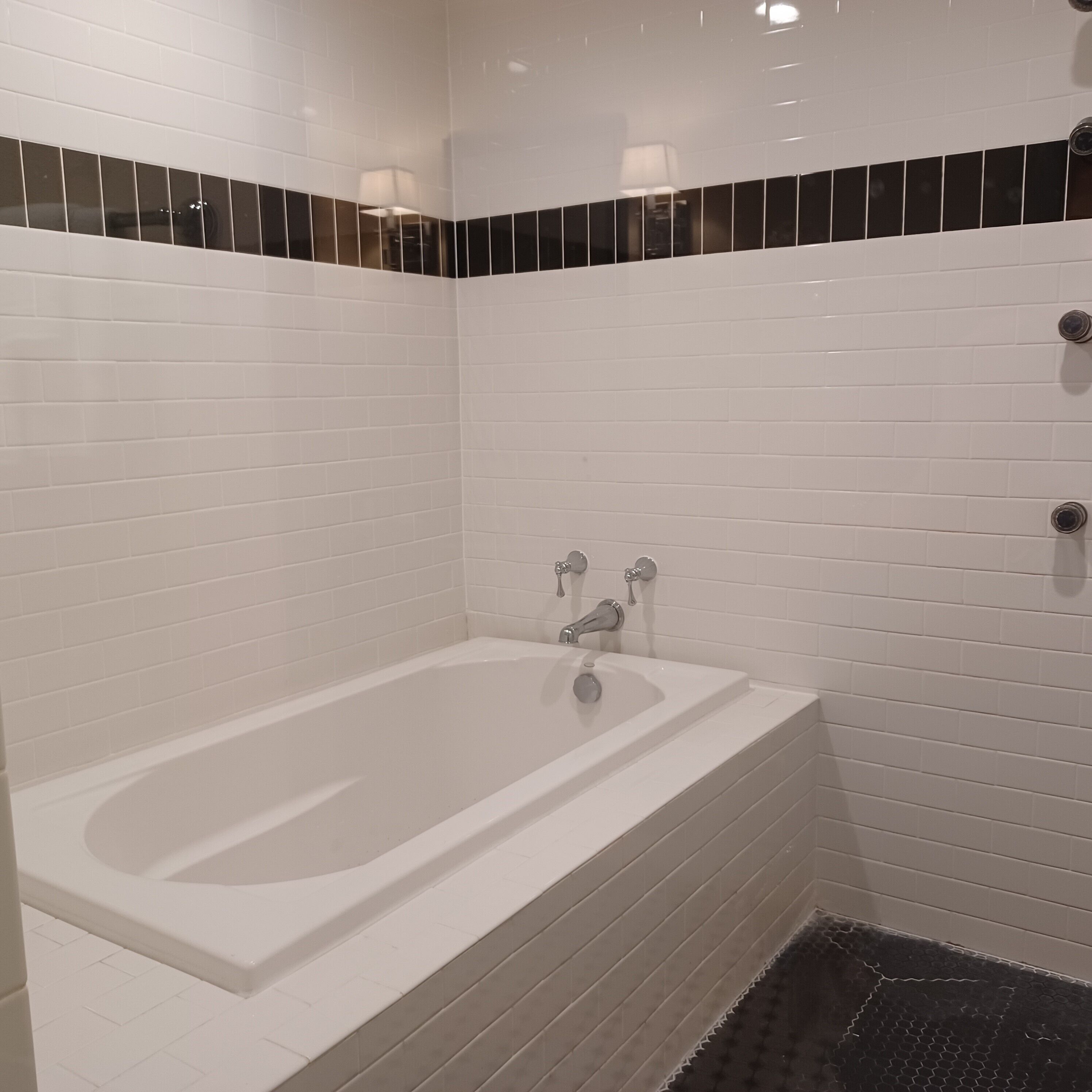 A modern bathroom with a white bathtub, black and white tiled walls, and a black textured floor.