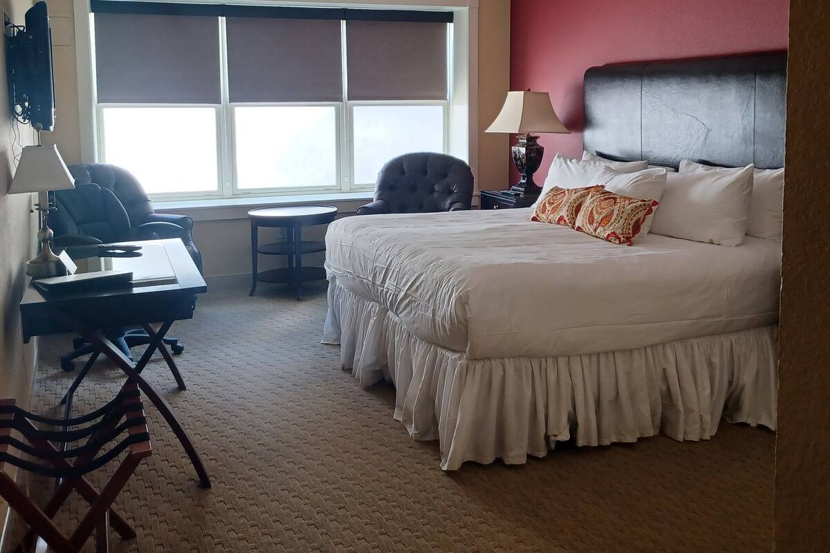 A hotel room with a bed, desk, chair, and a large window.