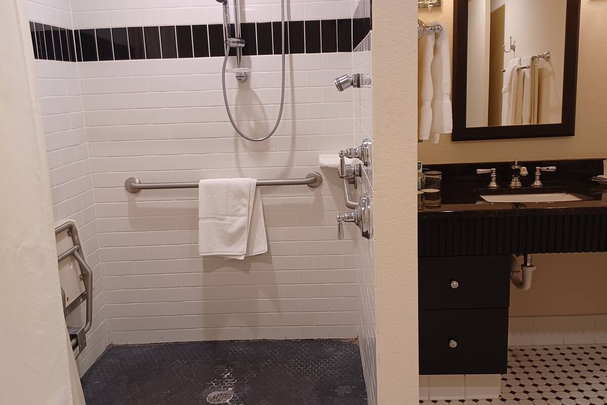 A bathroom with a black and white tiled floor, a white bathtub, a shower with a handheld showerhead, a towel rack, and a sink with a mirror above it.