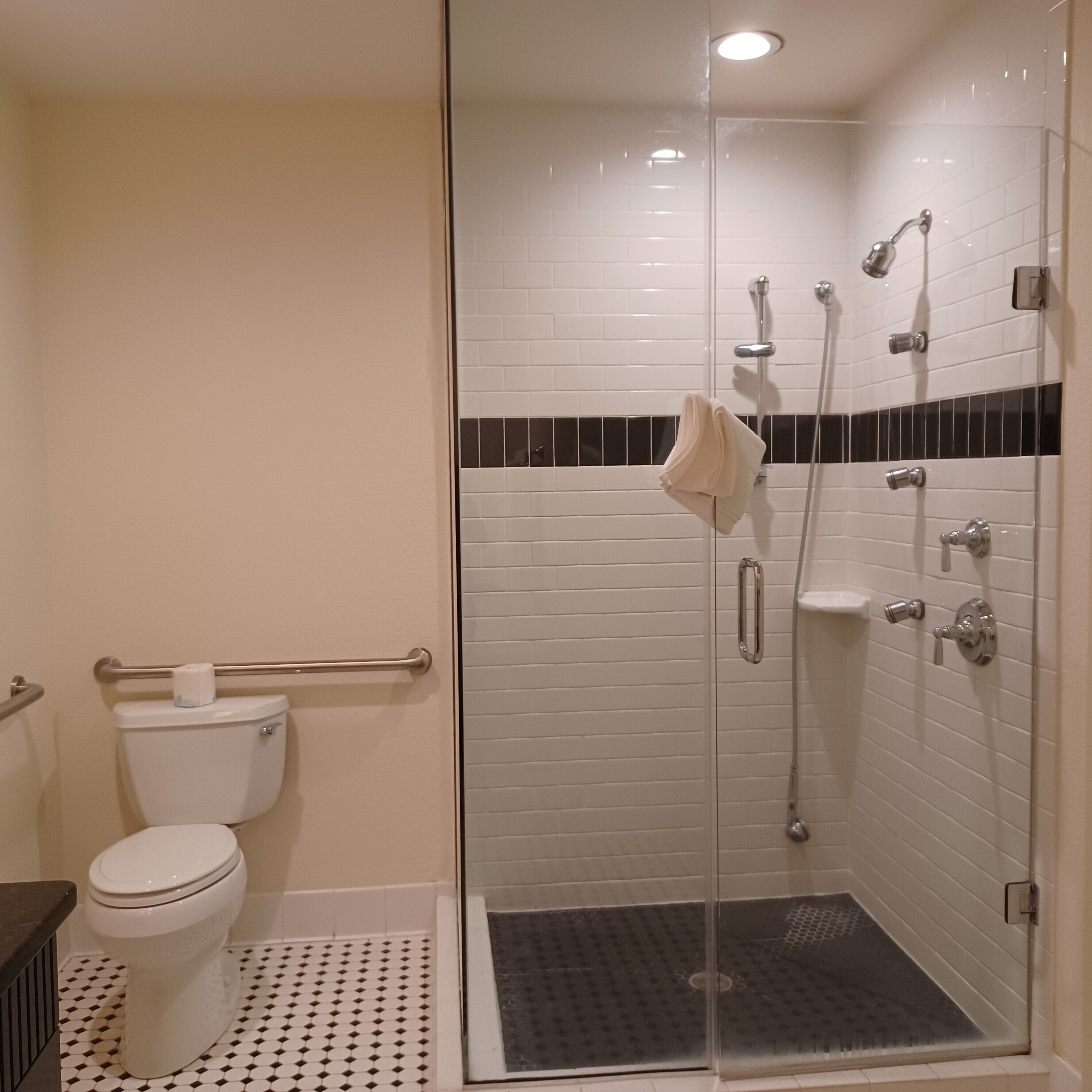 Un baño con inodoro, cabina de ducha con mampara de vidrio y piso de baldosas.