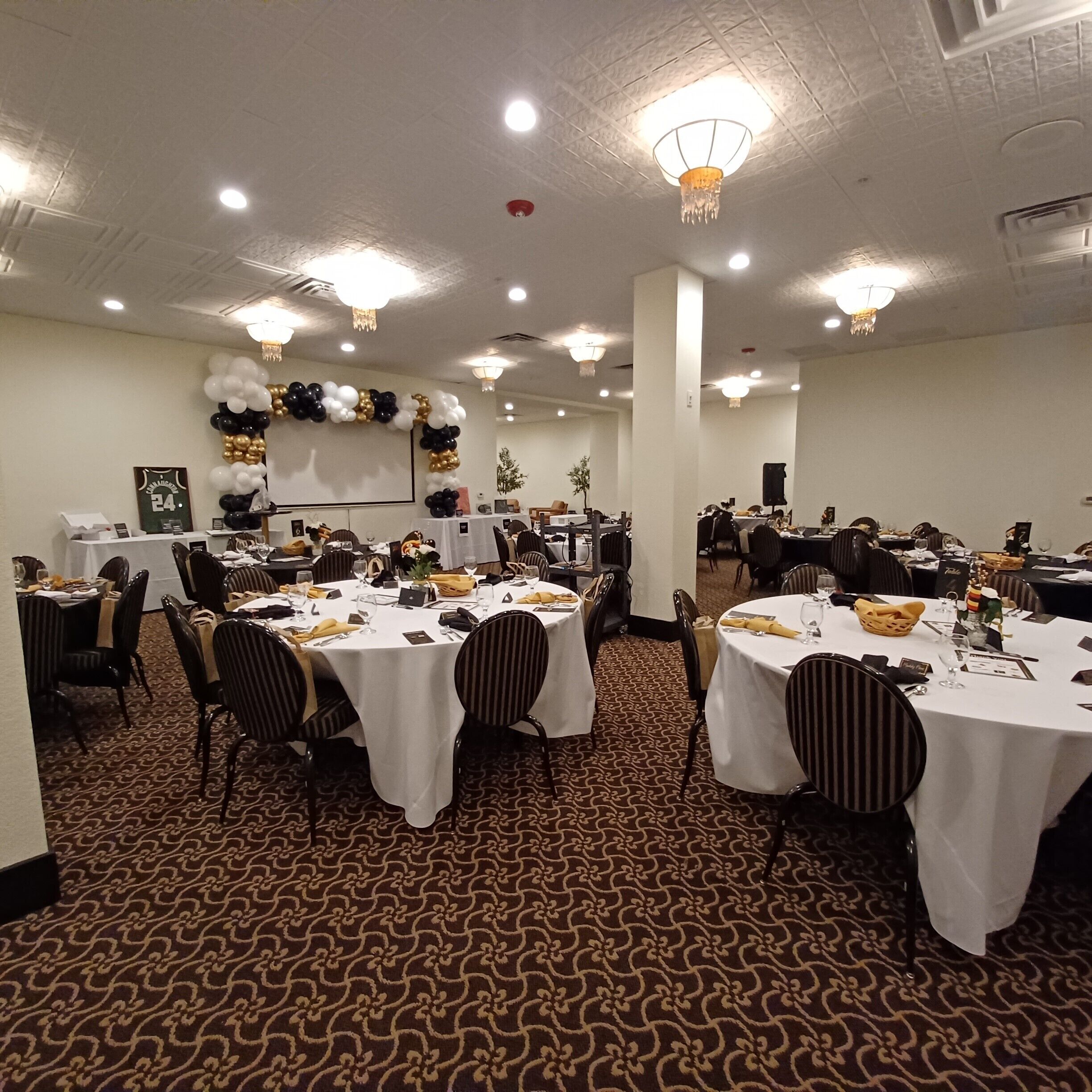 Une salle de banquet avec des tables rondes recouvertes de nappes blanches, disposées en rangées.