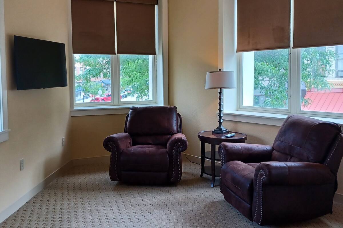 A room with two leather armchairs, a small table with a lamp, and a flat-screen TV mounted on the wall.