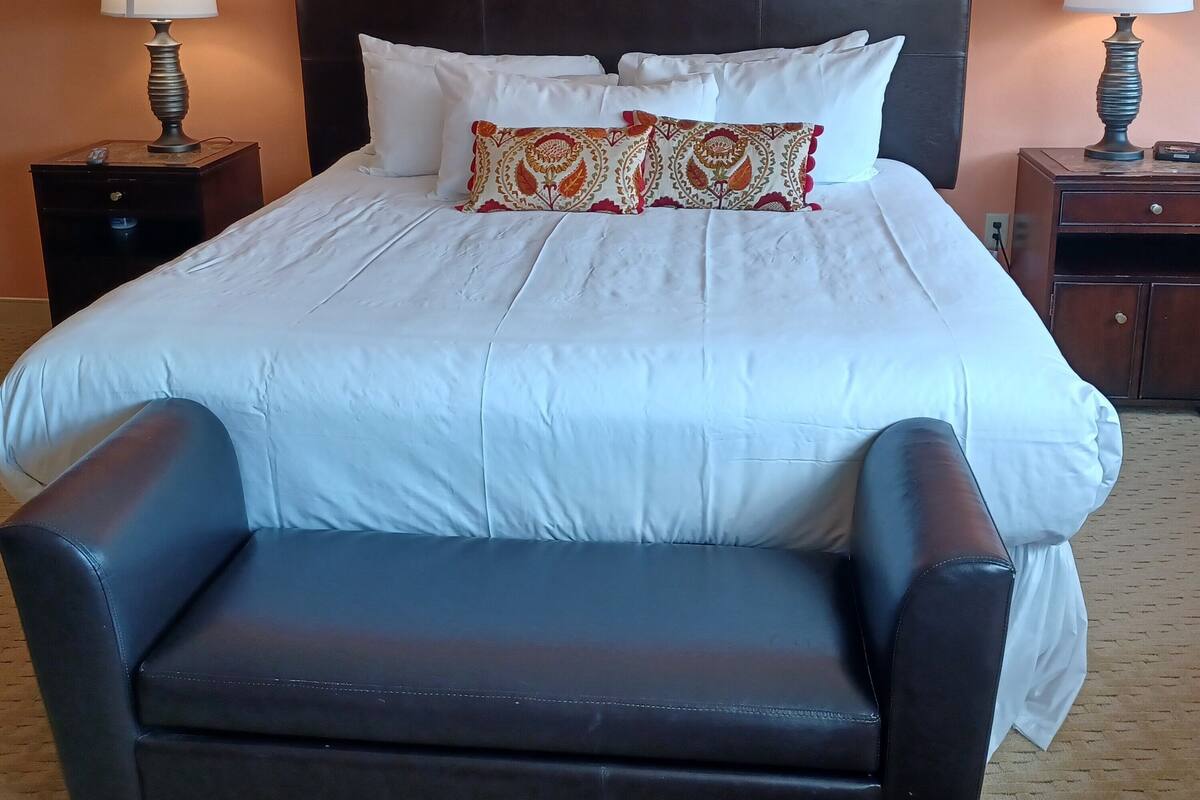 A hotel room with a large bed, two nightstands, a chair, and a patterned pillow.