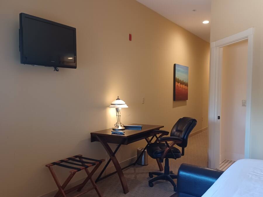 A hotel room with a bed, a desk with a chair, a TV mounted on the wall, and a painting on the wall.