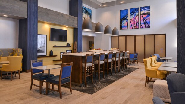 Un vestíbulo de hotel moderno con una larga mesa de comedor común, varias zonas de estar y obras de arte en las paredes.