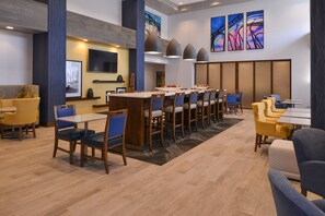 A modern hotel lobby with a long communal dining table, multiple seating areas, and artwork on the walls. - Hampton Inn & Suites Cincinnati-Mason (Mason)