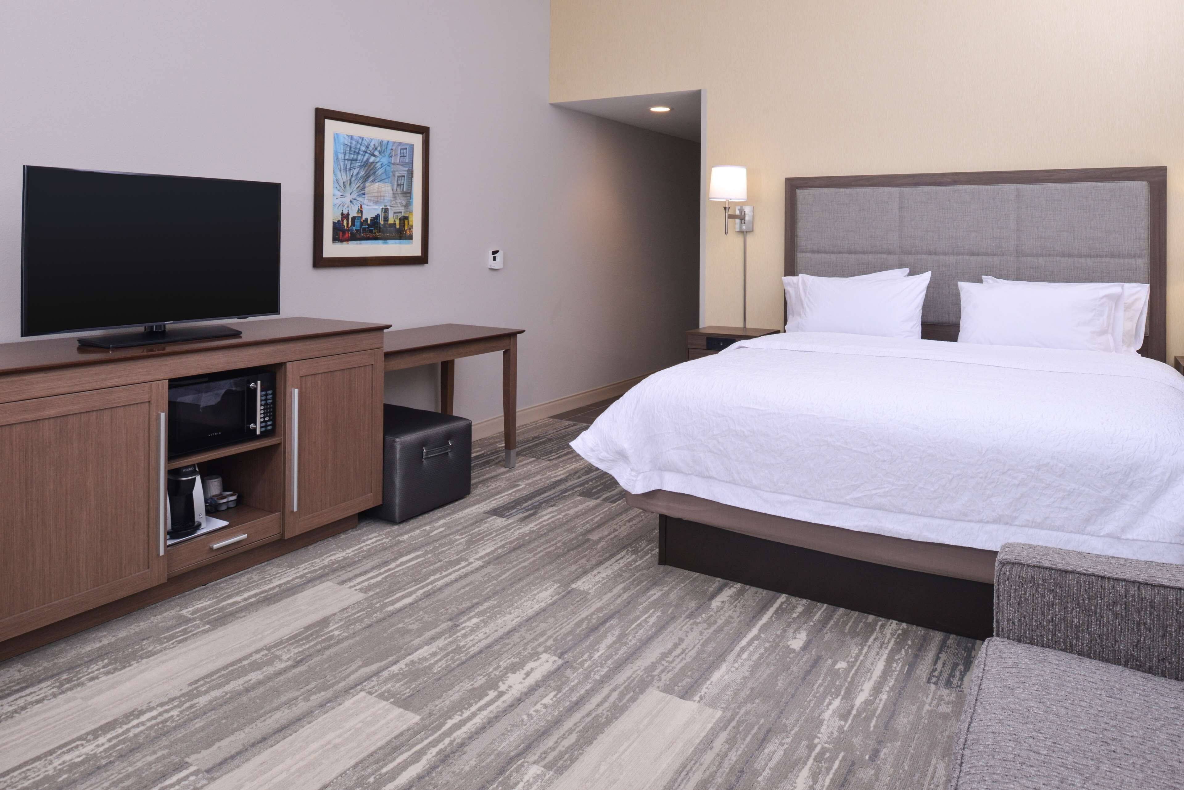 A hotel room with a bed, a TV, a microwave, a small table, and a picture on the wall.