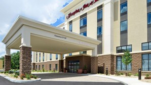Un hotel Hampton Inn & Suites con entrada cubierta, señalización clara y un área verde frontal.