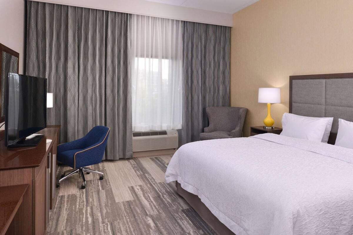 Une chambre d’hôtel avec un lit, un bureau avec une télévision, une chaise, une lampe et des rideaux.