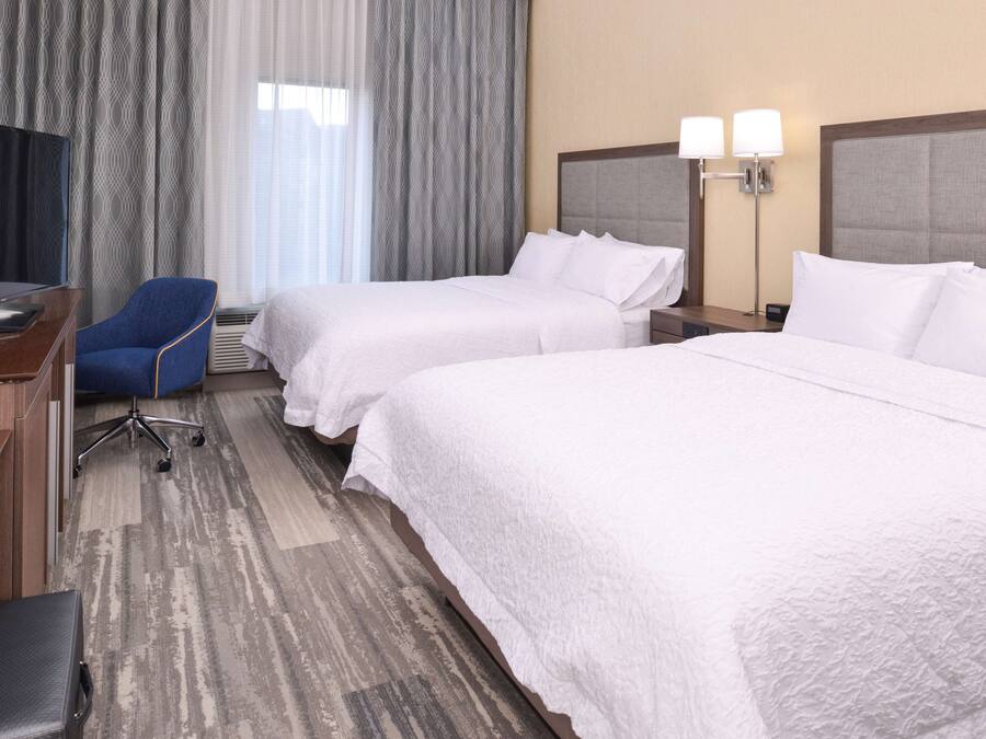 A hotel room with two beds, a desk with a computer, a chair, and a television.