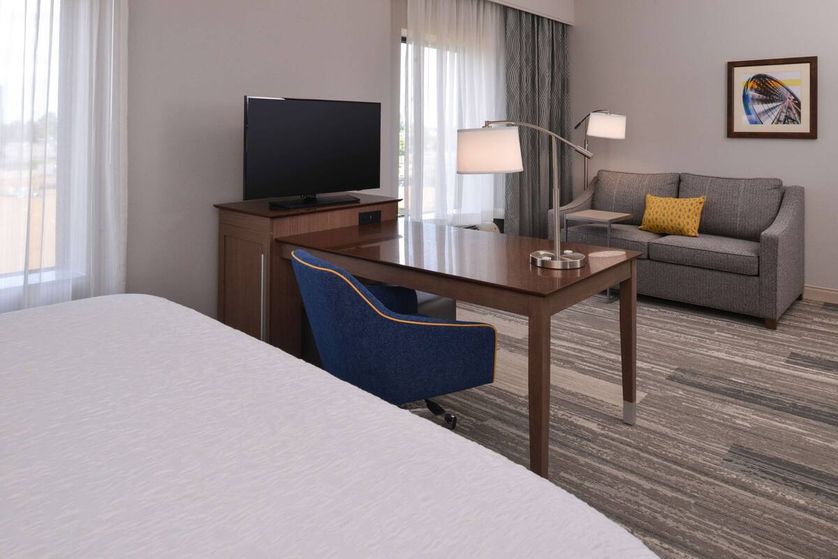 Une chambre d’hôtel comprenant un lit, un bureau avec une télévision, une chaise, un canapé avec un coussin et une lampe.