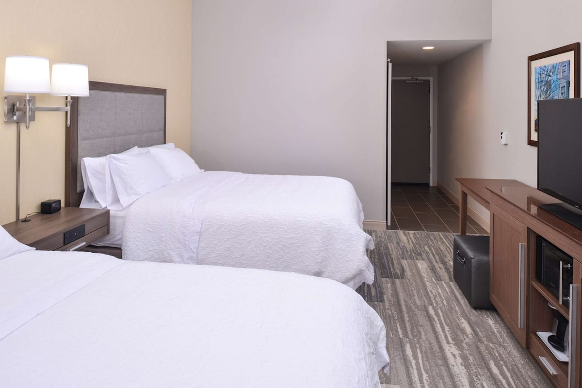 Une chambre d’hôtel avec deux lits, un bureau avec une lampe, une télévision et un petit placard.