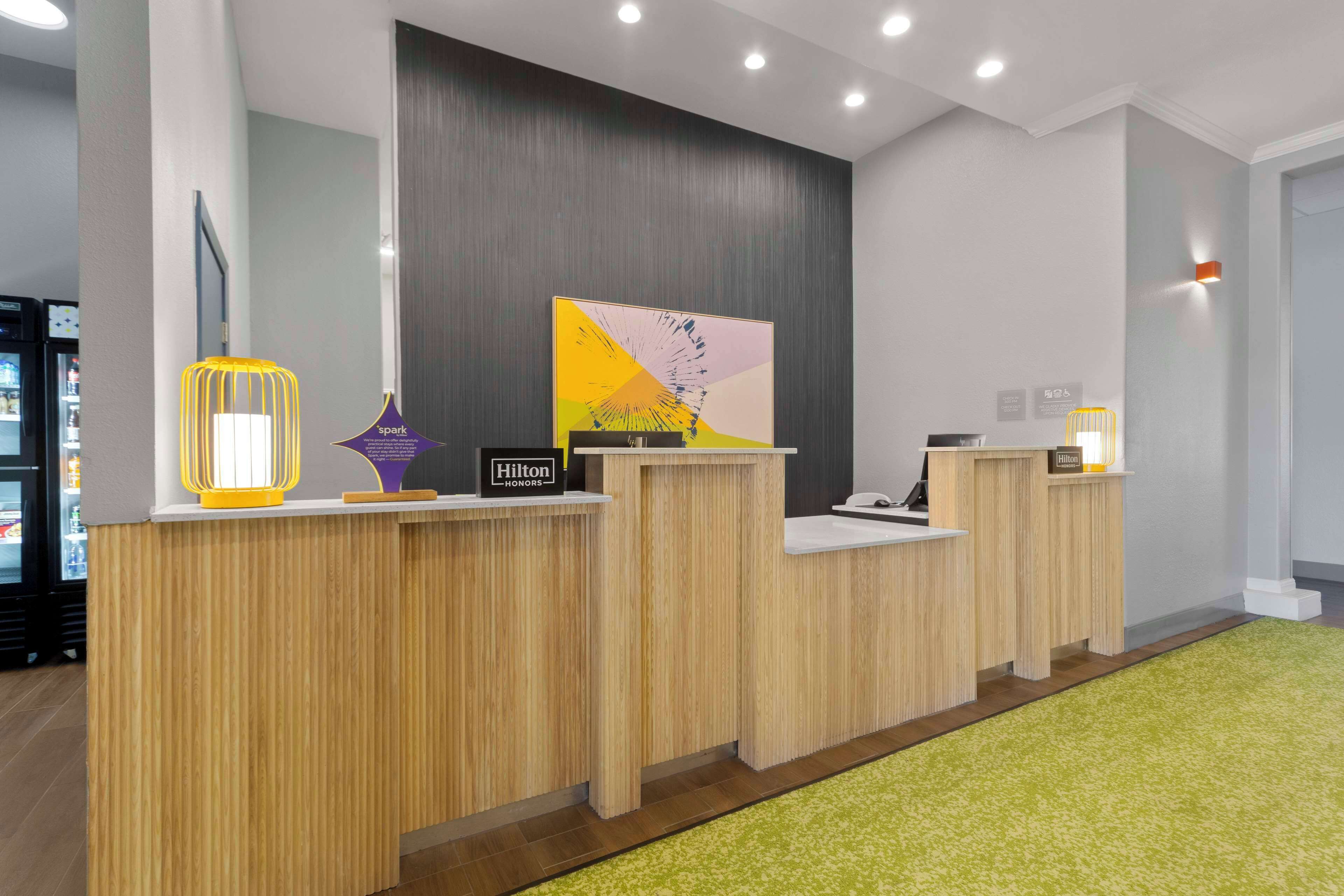 A hotel reception area with wooden reception desks, a large abstract painting, and a green carpet.
