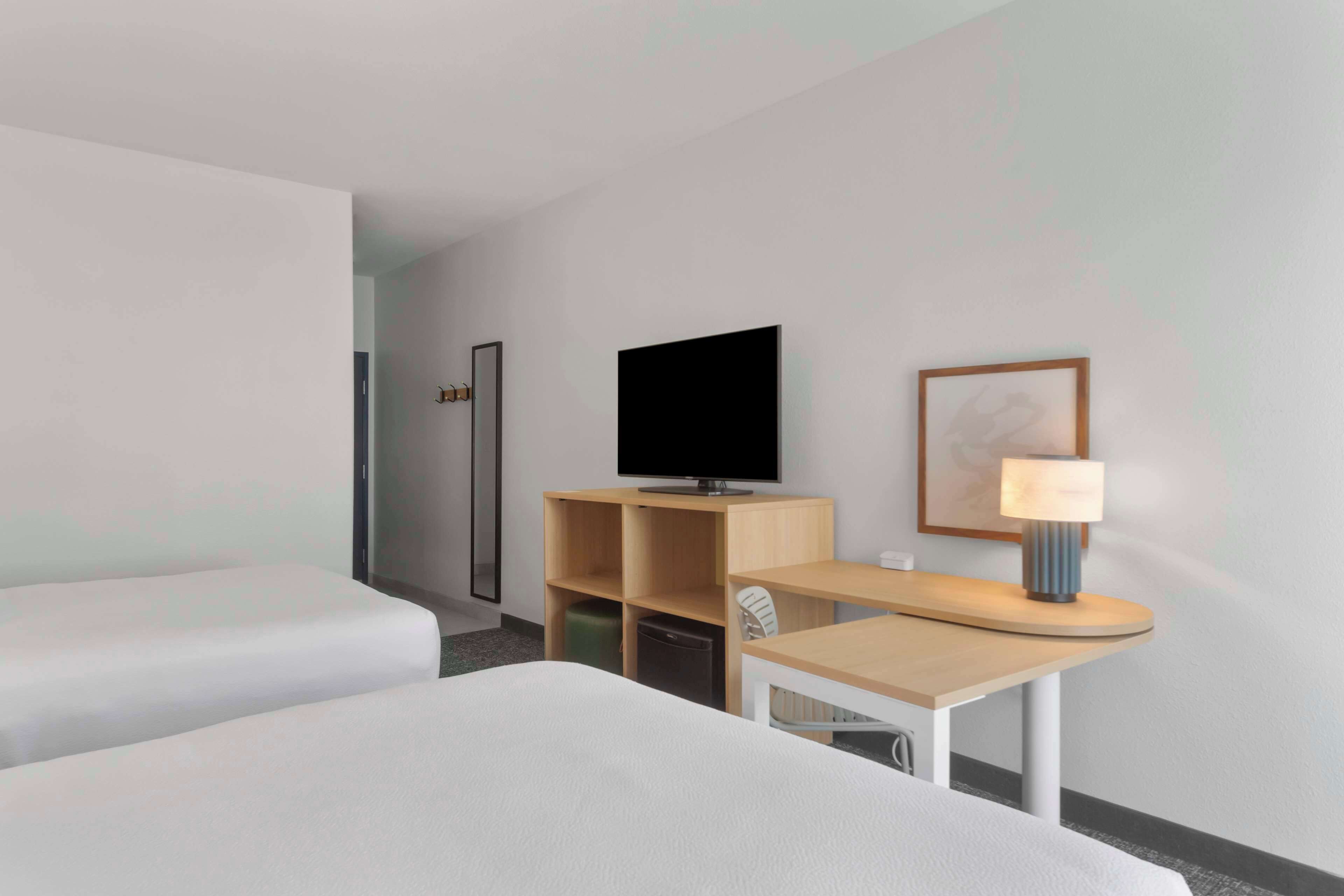 Habitación de hotel con cama, escritorio con lámpara, televisor y un cuadro en la pared.