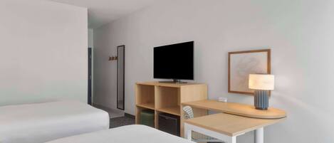 Habitación de hotel con cama, escritorio con lámpara, televisor y un cuadro en la pared.