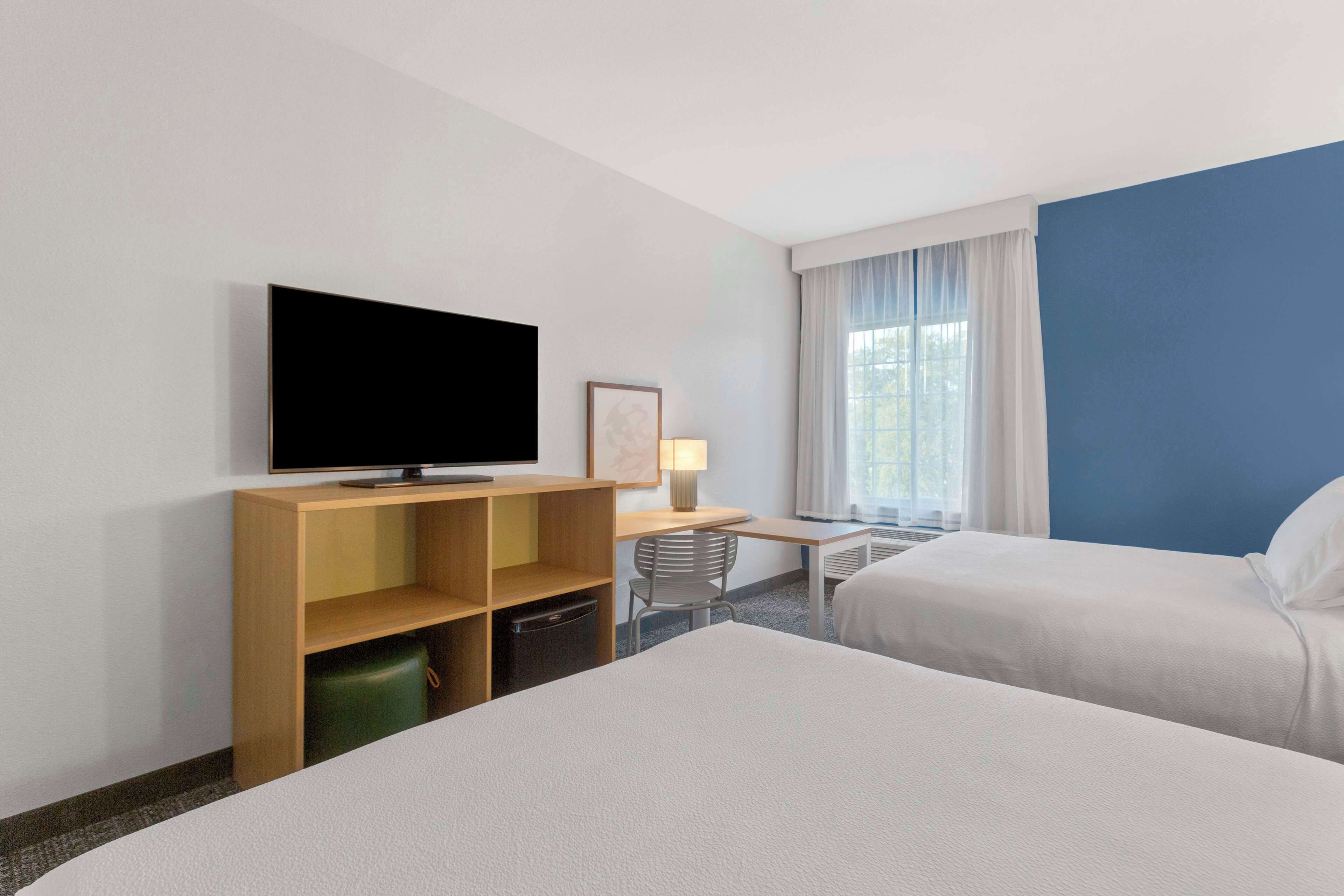 A hotel room with two beds, a desk, a television, and a window with curtains.