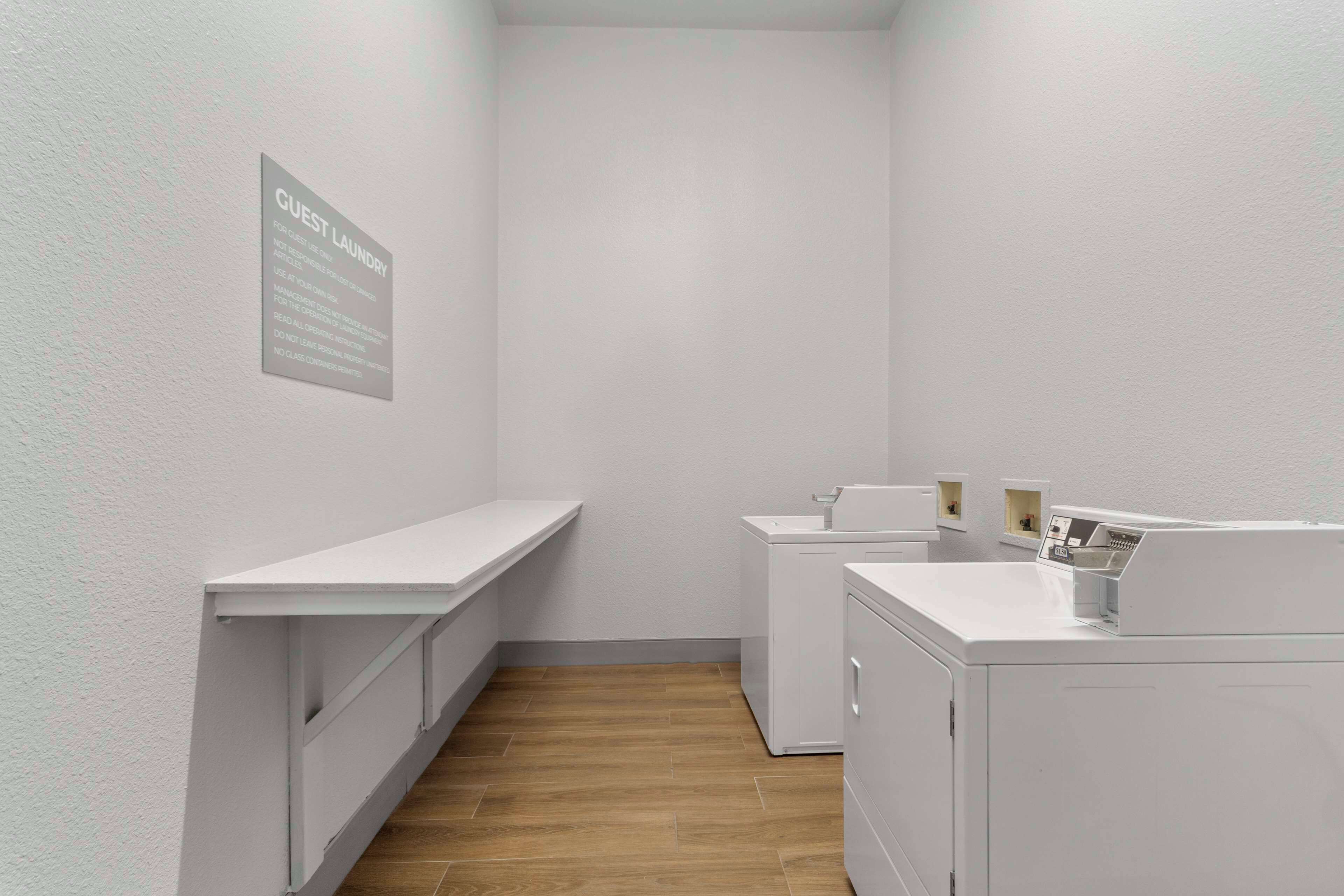 A compact guest laundry area with a white wall-mounted sign, a long white counter, and a washing machine.