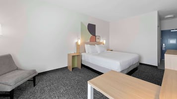 A hotel room with a bed, a desk, a chair, and a nightstand.