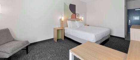 A hotel room with a bed, a desk, a chair, and a nightstand.