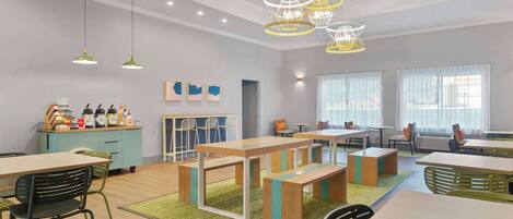 A modern dining area with wooden tables and benches, green chairs, and pendant lighting.