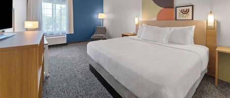 A hotel room with a large bed, a desk, a chair, a TV, and a window with curtains.