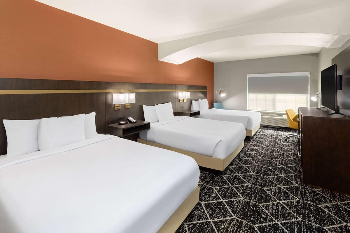 A hotel room with two beds, a desk, a TV, and a large window.