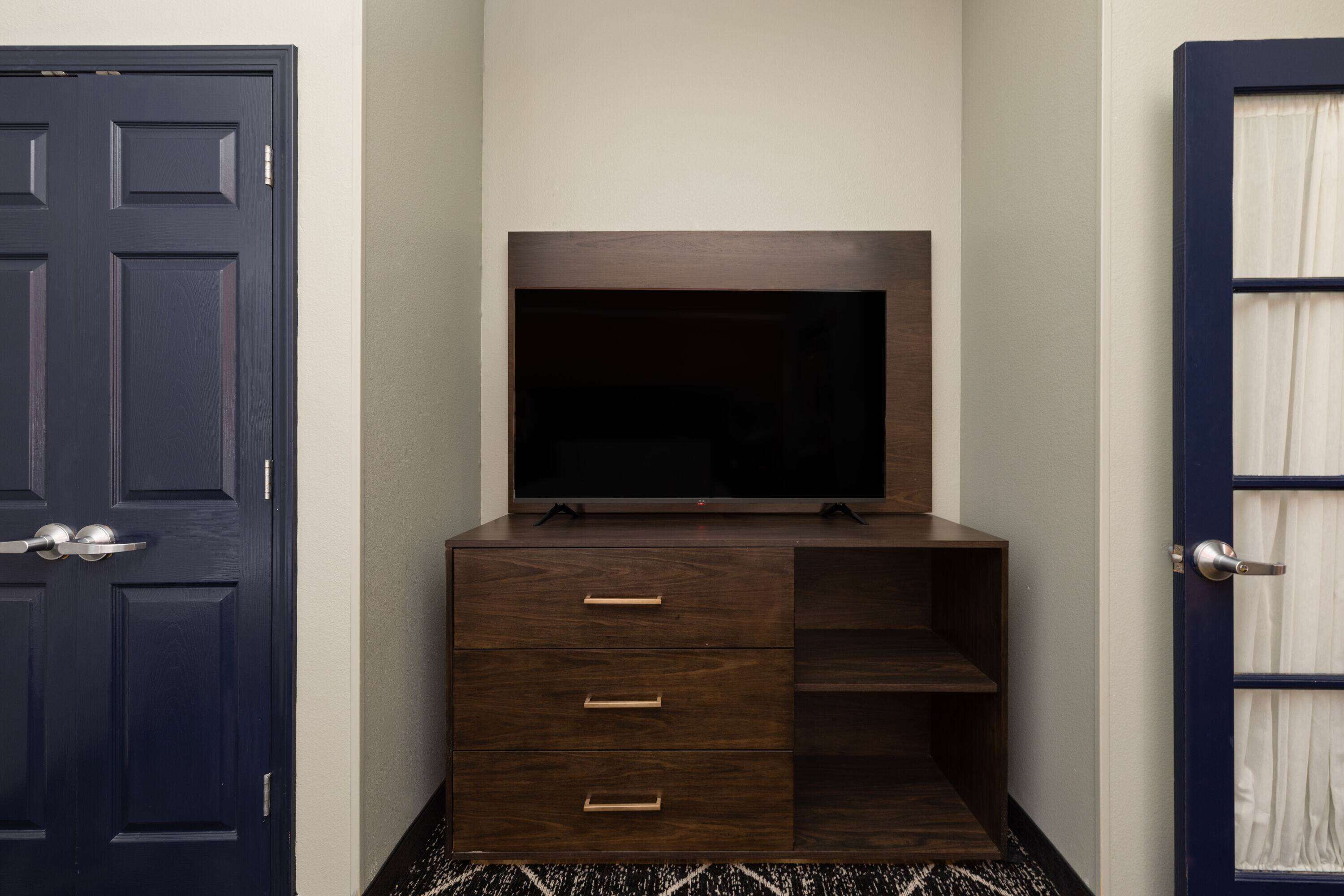 A dark wooden cabinet with a flat-screen TV on top, a door with a handle, and a patterned rug on the floor.