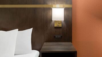 Habitación de hotel con cama, mesita de noche, lámpara de pared y panel de control.