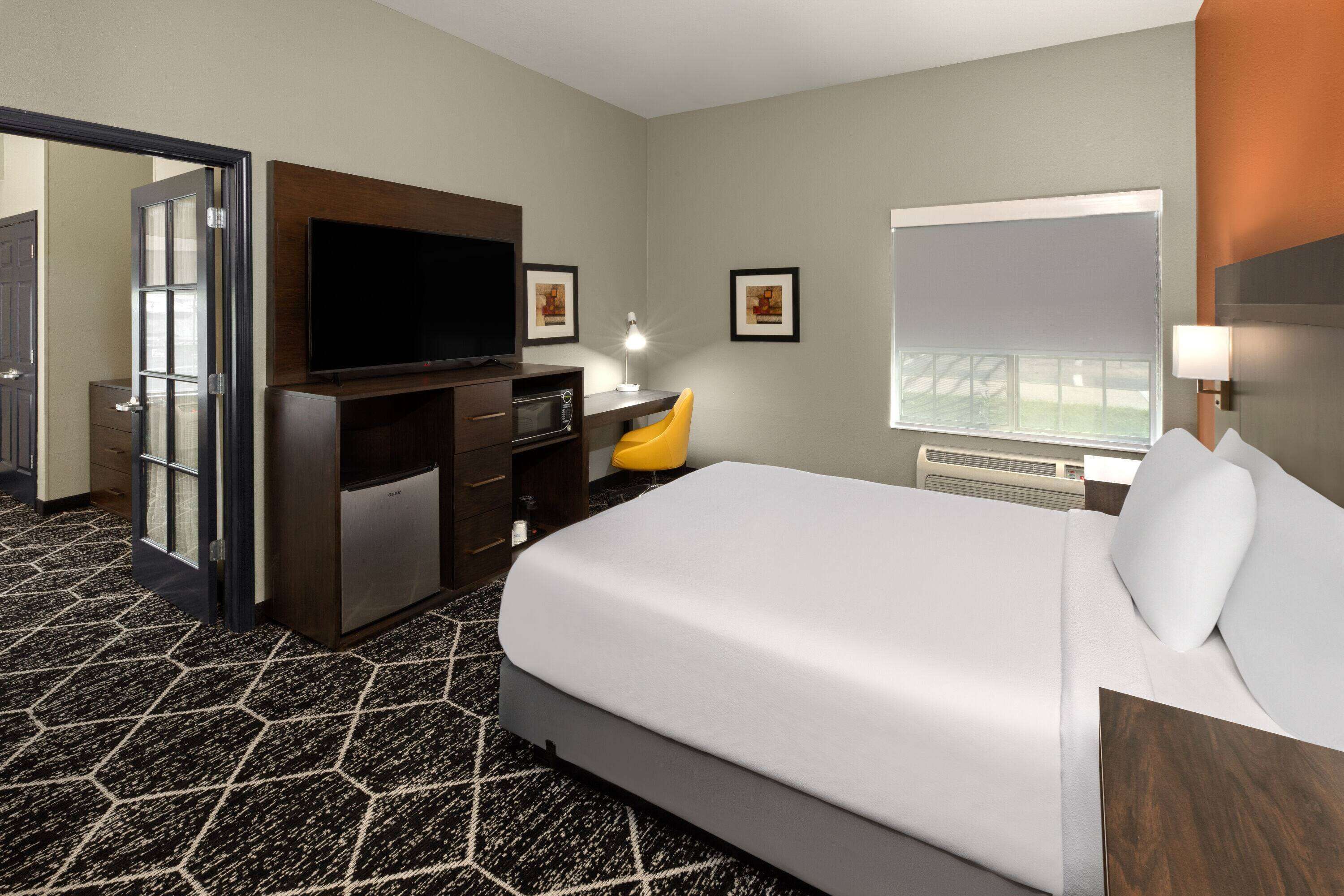 Une chambre d’hôtel dotée d’un grand lit, d’un bureau avec un téléviseur à écran plat, d’une lampe de bureau, d’une chaise, d’un four à micro-ondes et d’une grande fenêtre.
